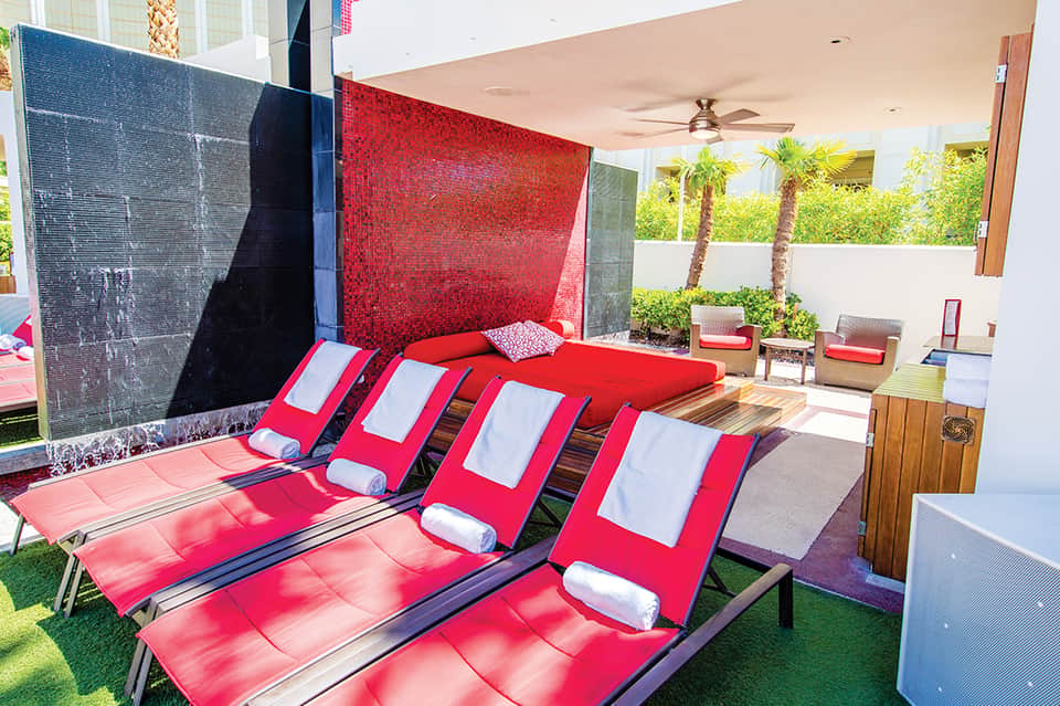 Outdoor spa lounge with red and white striped sun loungers, black accent walls, and palm trees