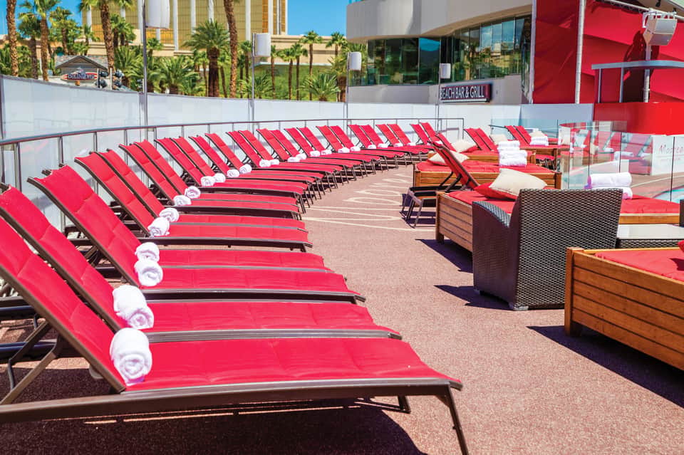 Rows of red lounge chairs with rolled towels on sunny beach club deck with palm trees