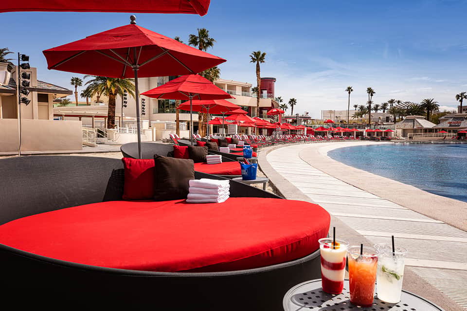 Luxury beachside resort with red umbrellas, lounge beds, and palm trees along curved pool deck