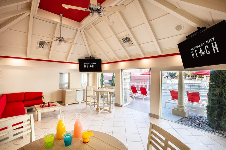 Bright interior lounge at Mandalay Bay Beach with red accents, ceiling fans, and glass doors opening to poolside area