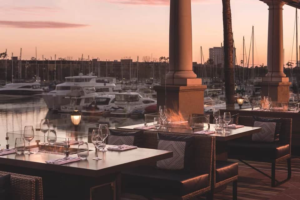 Waterfront dining terrace at sunset with sailboats and marina views from covered seating area