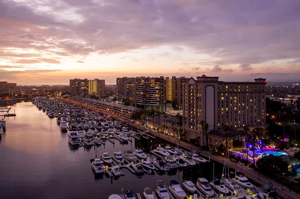 Marina at dusk with moored boats, waterfront hotels, and colorful pool lights reflecting on calm water