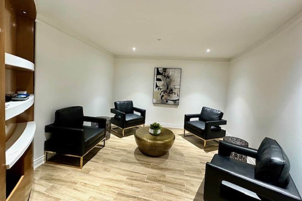 Contemporary lounge area with black leather chairs arranged around a gold bowl table and wooden shelving