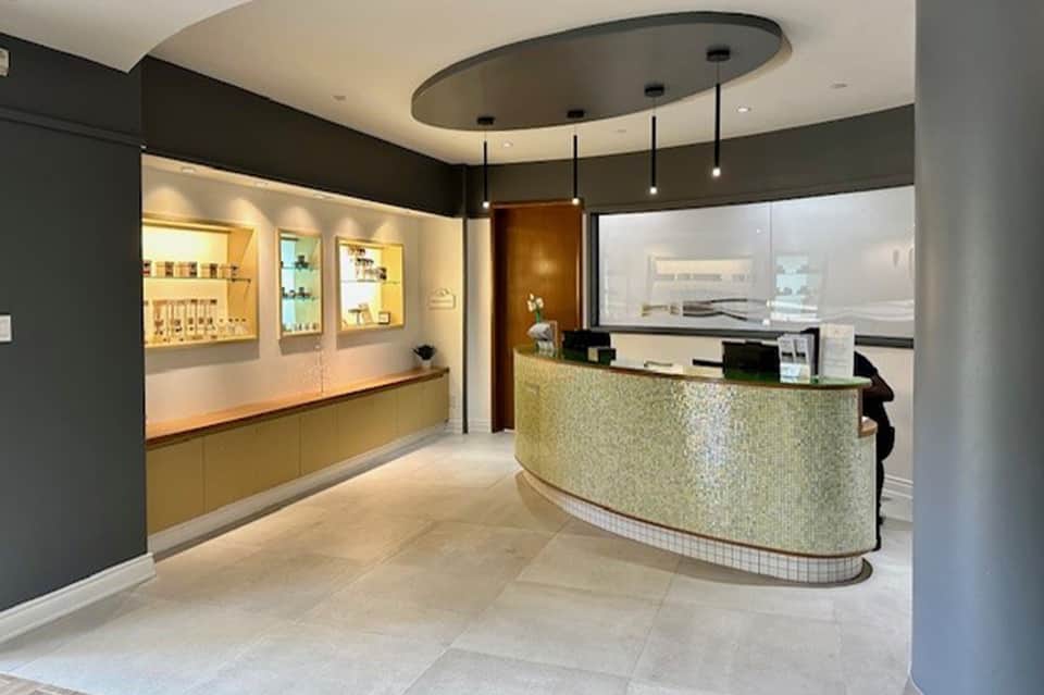 Modern spa reception area with curved mosaic counter, illuminated product displays, and sleek black and gold interior design