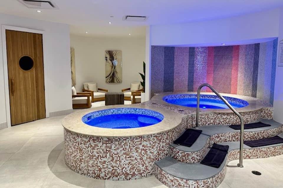 Luxury spa with two illuminated blue hot tubs, mosaic tile surrounds, and lounge seating area