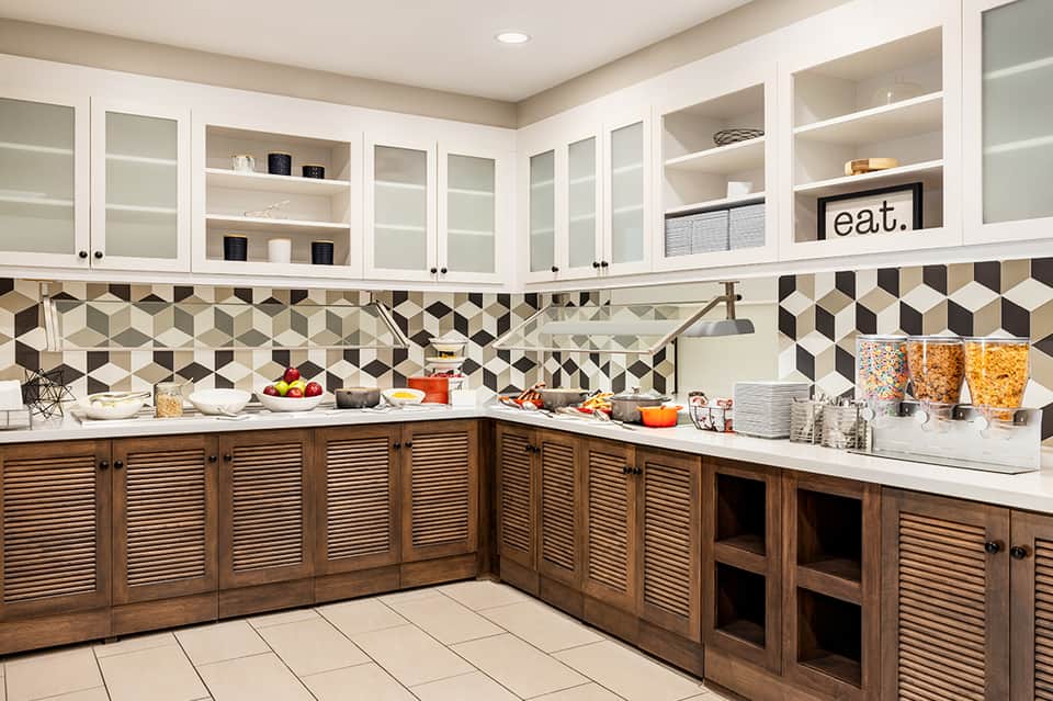 Modern kitchen with white upper cabinets, geometric backsplash, and wood louvered lower cabinets