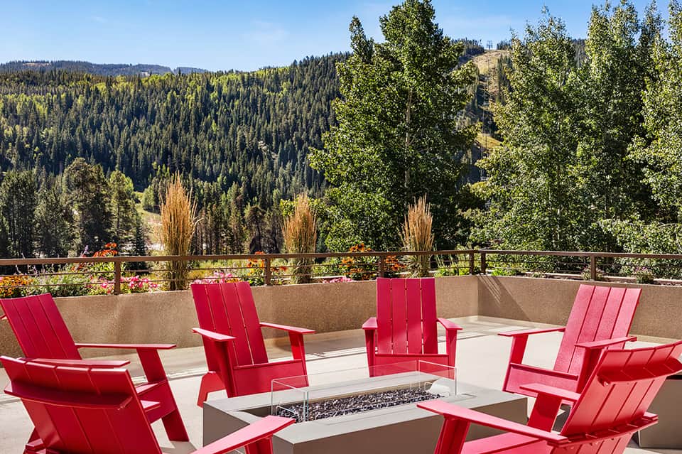 Red Adirondack chairs arranged around a fire pit on a terrace with mountain and forest views