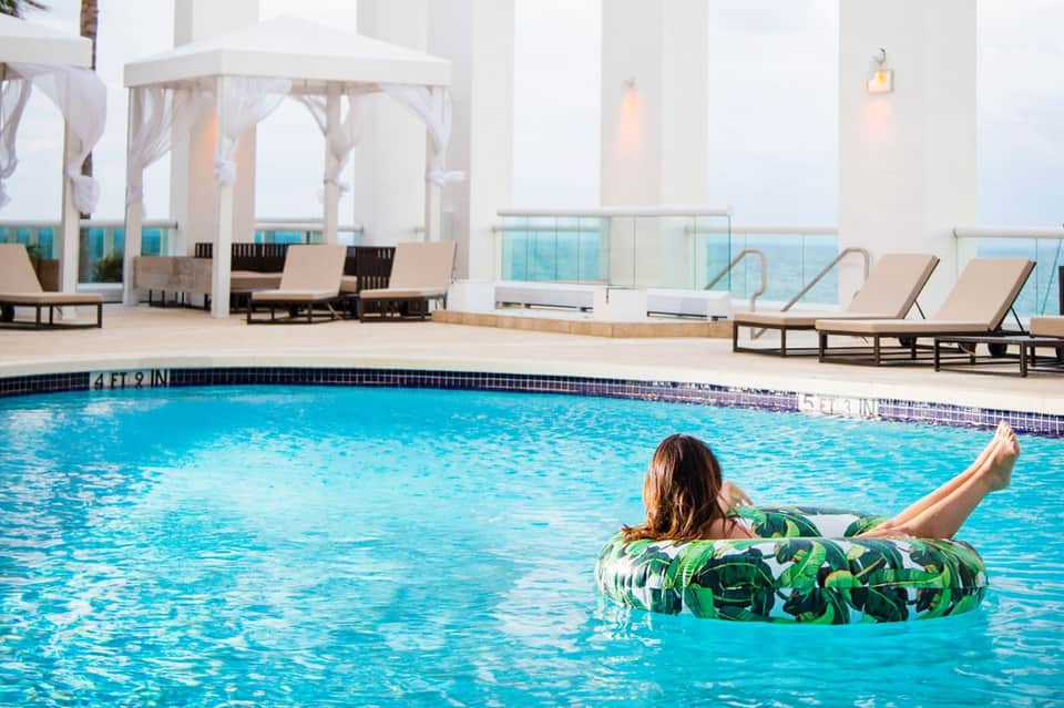Woman floating on patterned tube in resort pool with lounge chairs