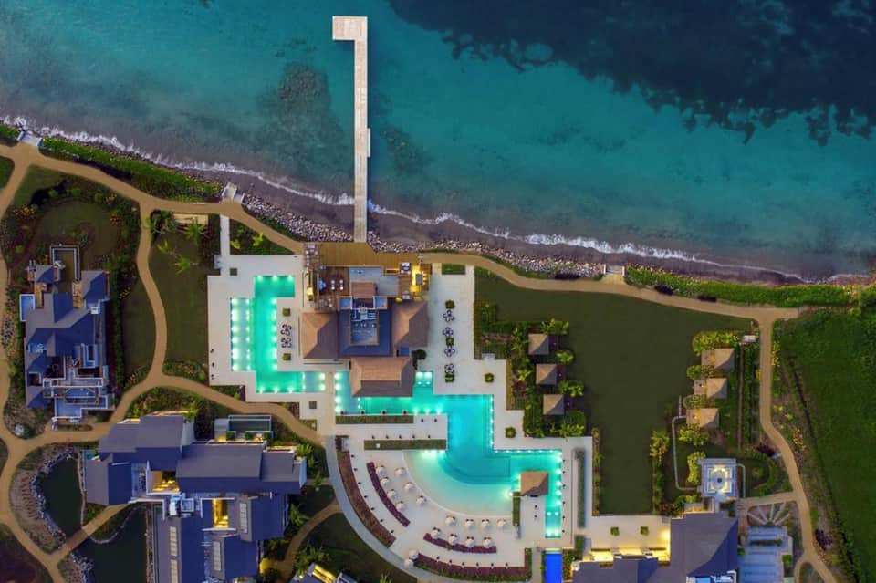 Aerial view of luxury beachfront resort with illuminated turquoise pools and manicured grounds along pristine coastline