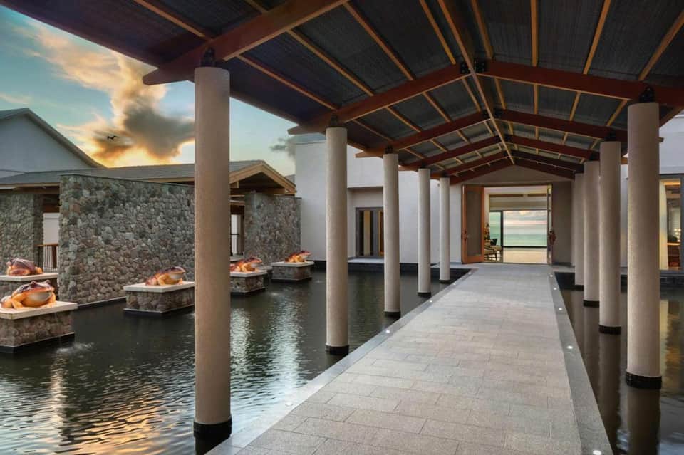 Modern covered walkway with columns over reflecting pools, stone walls, and sunset sky view