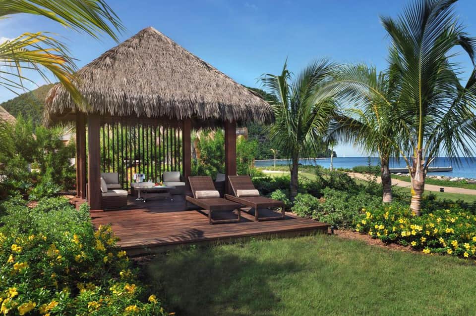 Thatched-roof beachside pavilion with lounge seating overlooking turquoise ocean and palm trees