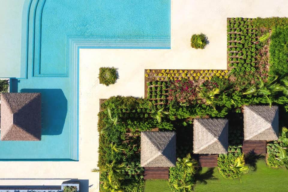 Aerial view of resort pool with turquoise water, lounge chairs, and manicured gardens with umbrella shade structures