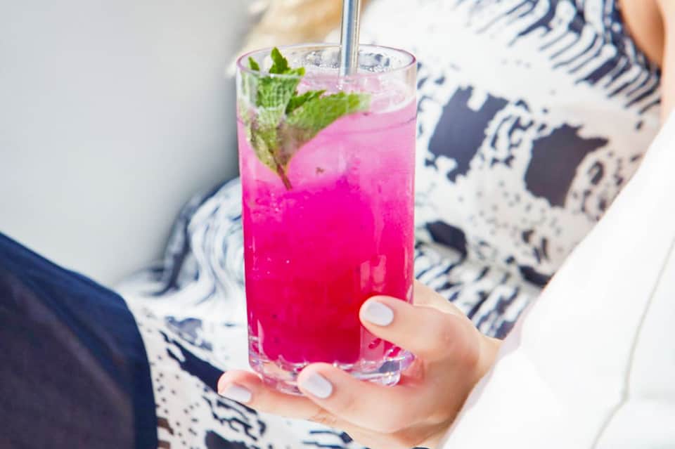 Woman holding vibrant pink cocktail with mint garnish and straw, wearing striped top