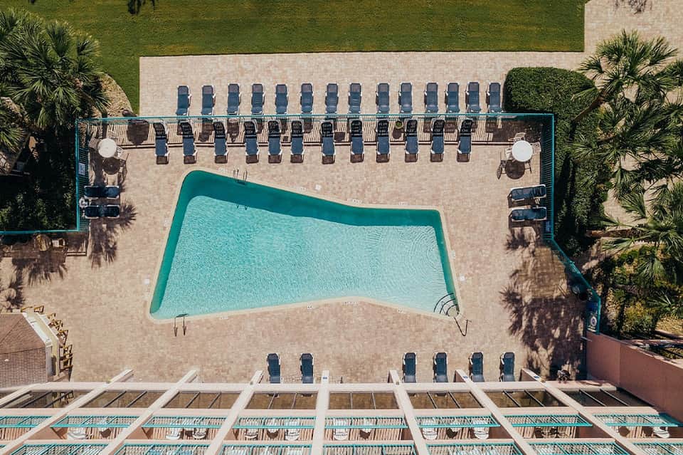 Overhead view of resort pool with lounge chairs arranged on beige patio surrounded by manicured grass
