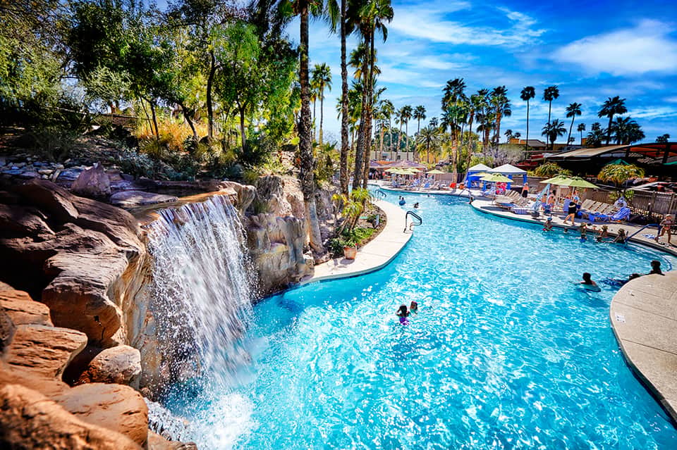 Resort pool with cascading waterfall, palm trees, and guests swimming in crystal-clear turquoise water
