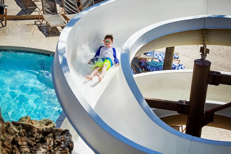 Child sliding down white water slide into turquoise pool at resort