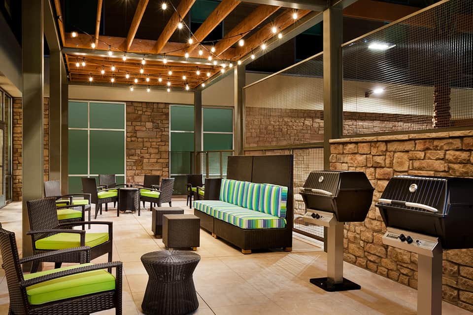 Outdoor patio with string lights, lounge seating, striped cushions, stone walls, and grills at night