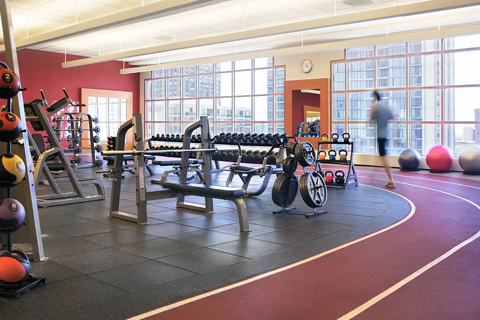 Modern fitness center with exercise equipment, dumbbells, medicine balls, and floor-to-ceiling windows