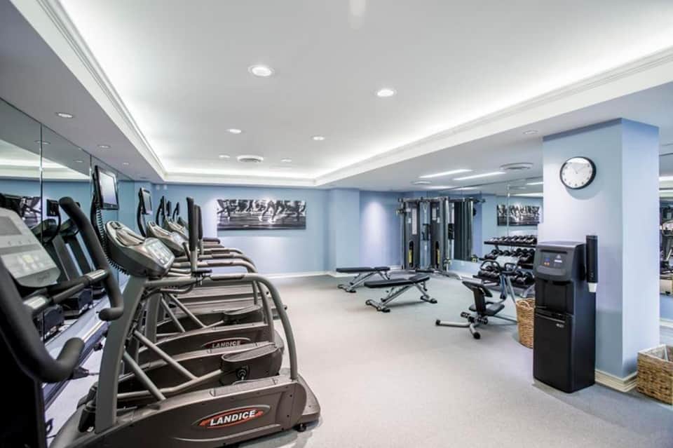 Modern fitness center with cardio equipment, strength machines, and mirrored walls in bright blue interior