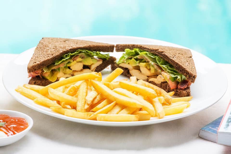 Whole wheat sandwich with lettuce and tomato served with french fries on white plate