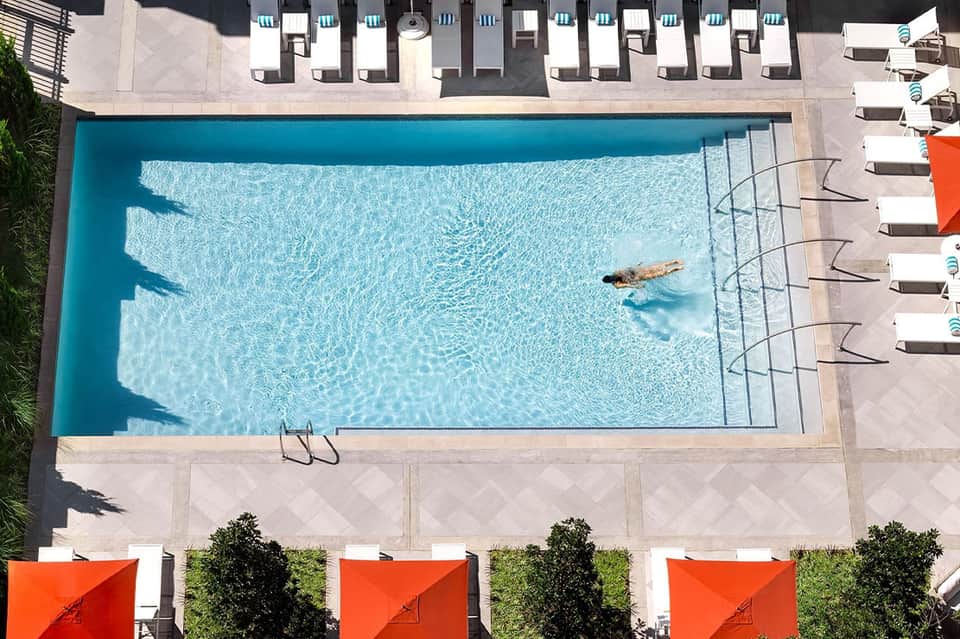 Overhead view of rectangular swimming pool with two swimmers and white lounge chairs on surrounding deck