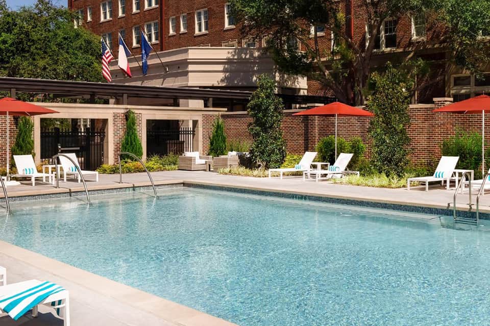 Resort outdoor pool with lounge chairs, red umbrellas, and brick building facade with ivy