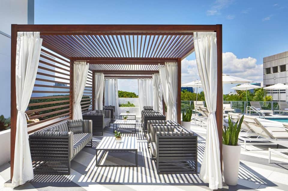 Modern pergola lounge area with striped seating, white curtains, and ocean views at resort