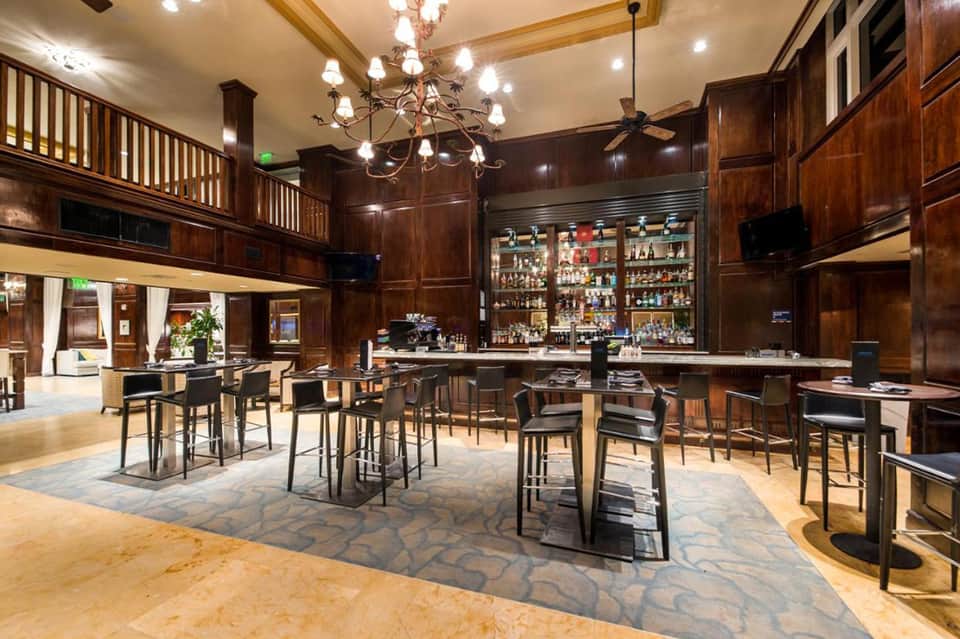 Elegant hotel bar lounge with dark wood paneling, crystal chandelier, and multiple bar seating areas