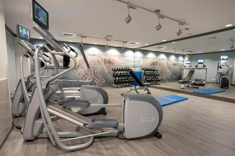 Modern fitness center with cardio equipment, dumbbells, blue exercise mats, and motivational wall mural