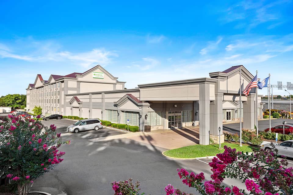 Hotel entrance with burgundy awnings, manicured flowers, and American flag in daylight