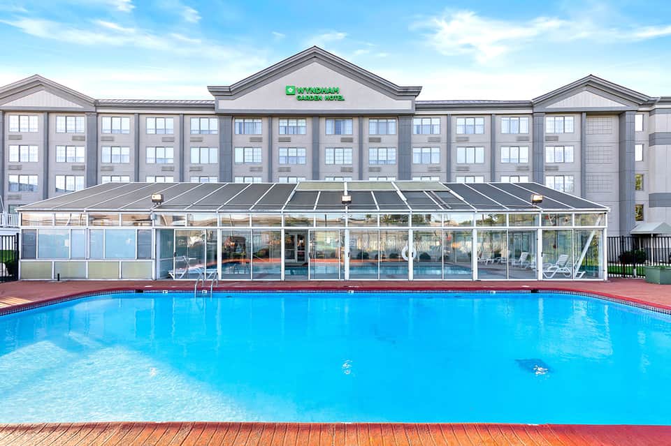 Outdoor heated pool with glass enclosure and multi-story hotel building in background under blue sky