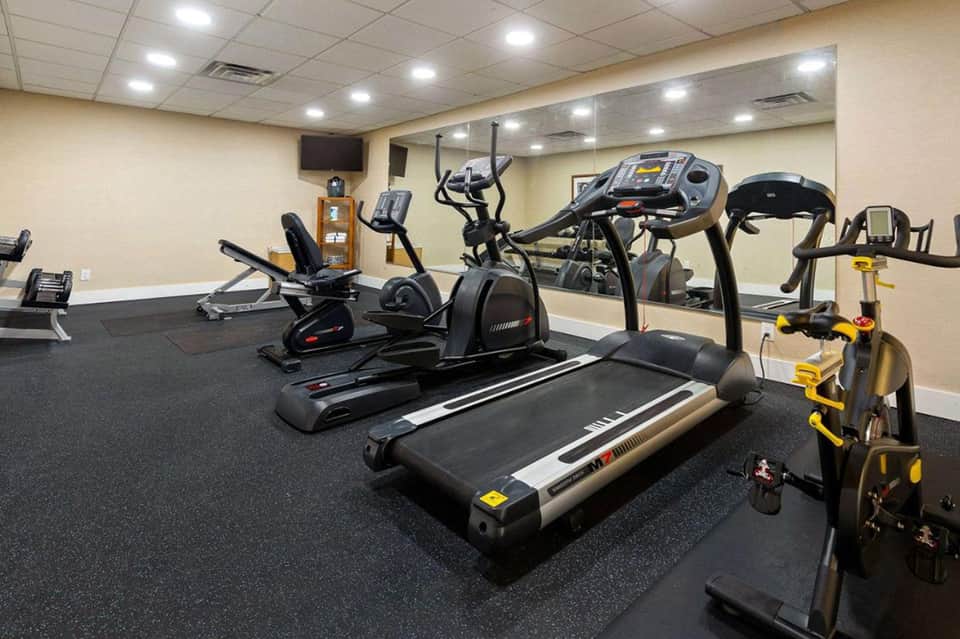Fitness center with treadmills, exercise bikes, elliptical machines, and black rubber flooring