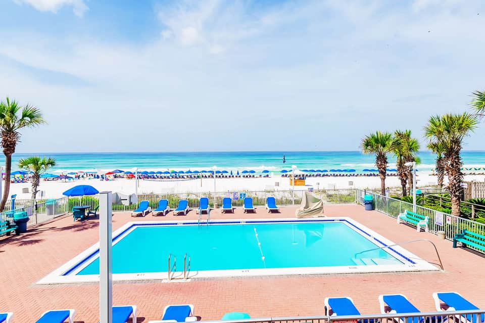 Beachfront resort pool with blue loungers, palm trees, and ocean view with sandy beach and cabanas