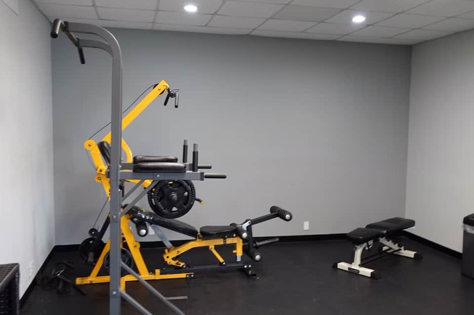 Modern fitness center with yellow exercise equipment, treadmills, and weight benches on dark flooring
