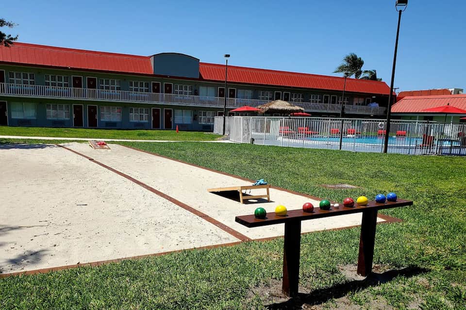 Outdoor cornhole game and bocce ball setup on sandy court with resort building and pool in background