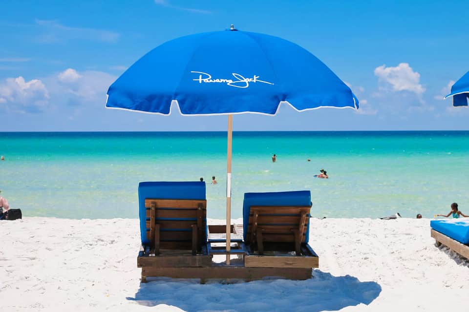 Blue beach umbrella with two loungers on white sand overlooking turquoise ocean water