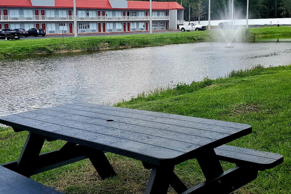 Black picnic table on grass overlooking pond with fountain and red-roofed motel building