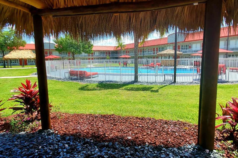 Tiki-roofed pavilion overlooking resort pool and manicured grounds with red-roofed buildings