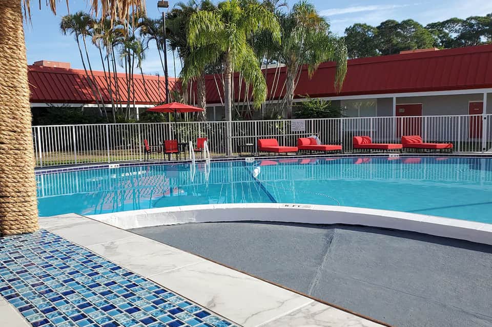 Resort pool with turquoise water, red lounge chairs, and palm trees surrounded by fencing