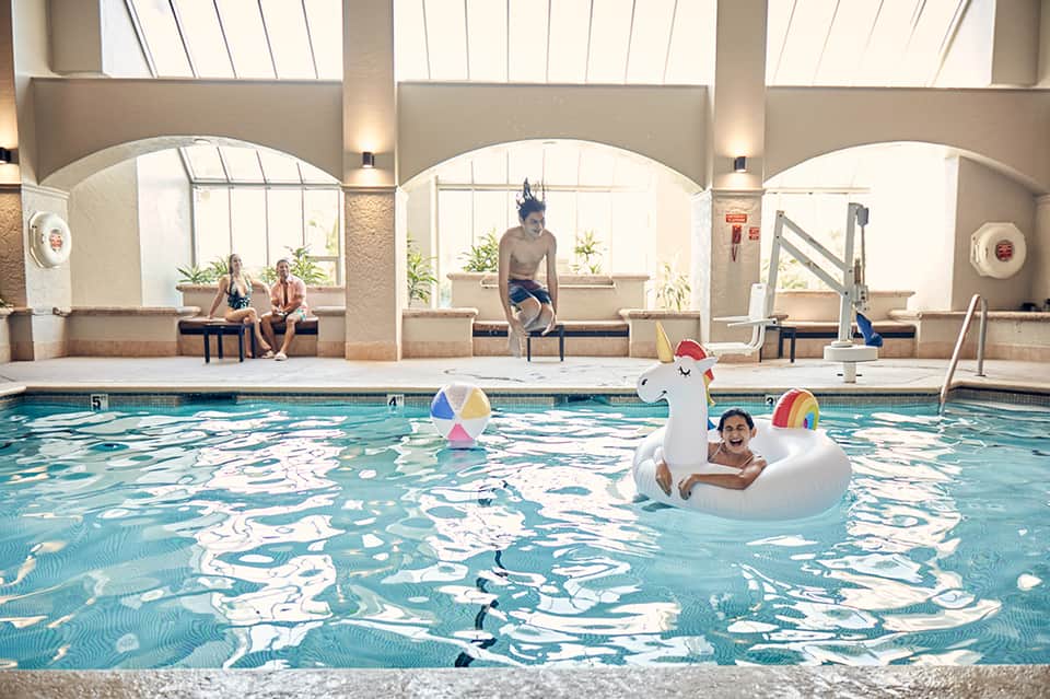 Indoor swimming pool with children playing on inflatable unicorn float, arched windows above