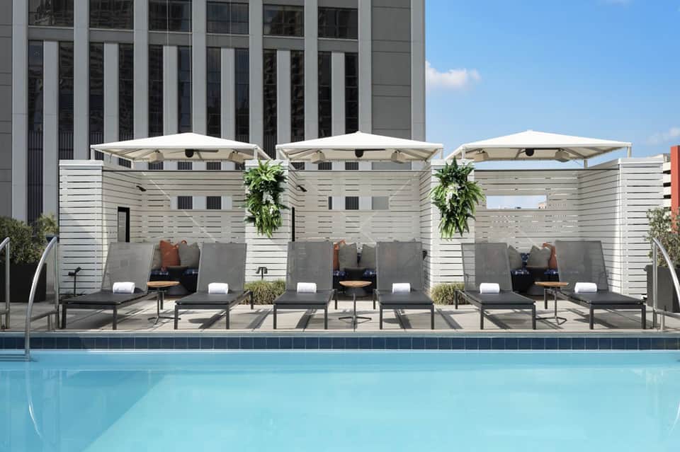 Modern hotel pool deck with three white cabanas, lounge chairs, and umbrellas overlooking a turquoise pool