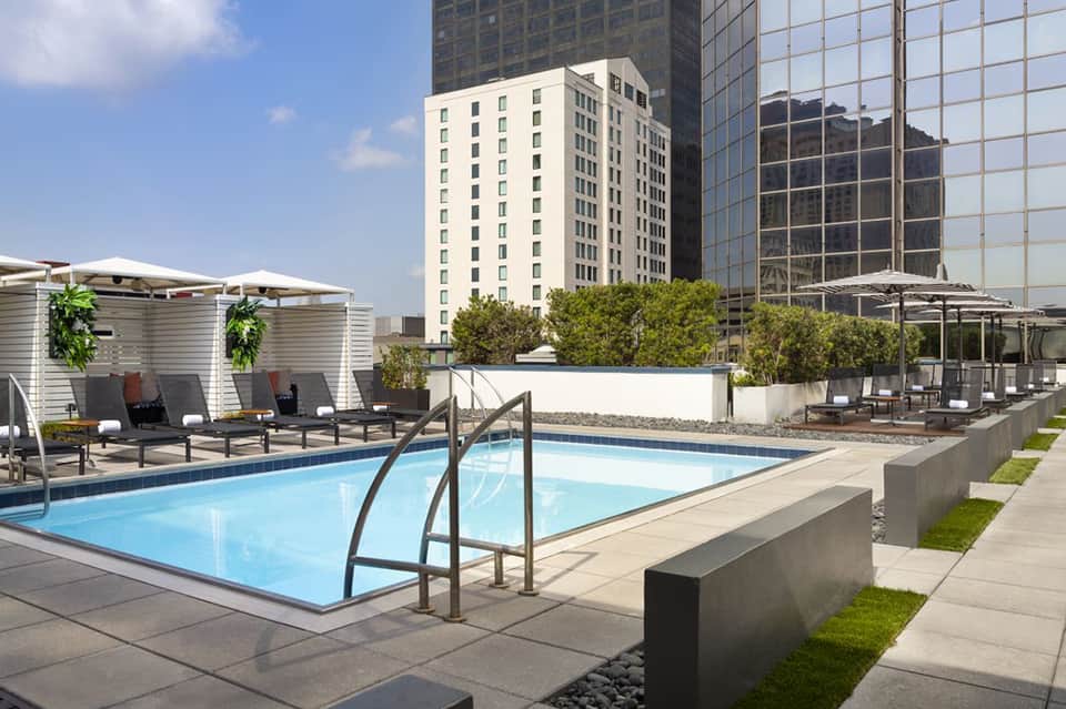 Rooftop pool deck with lounge chairs, umbrellas, and city skyscrapers in background