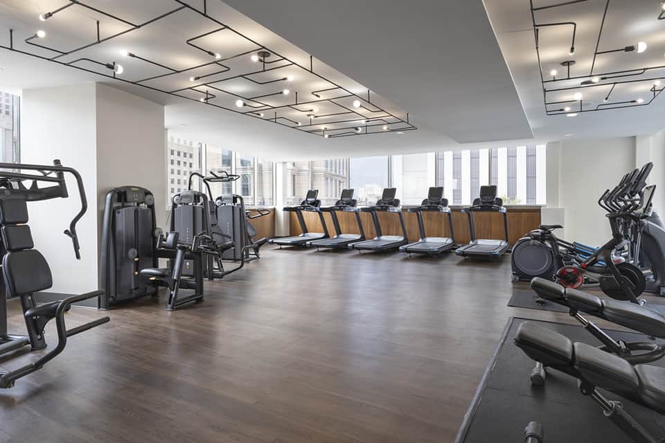 Modern gym with cardio machines, weight equipment, and floor-to-ceiling windows overlooking city skyline
