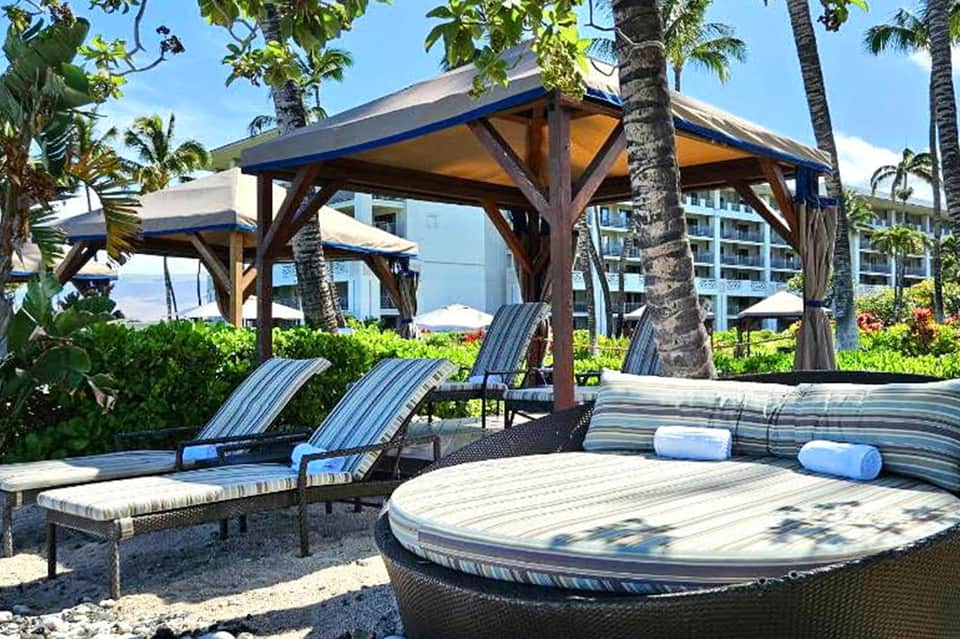 Beachfront lounge area with striped chairs under wooden pergolas and palm trees