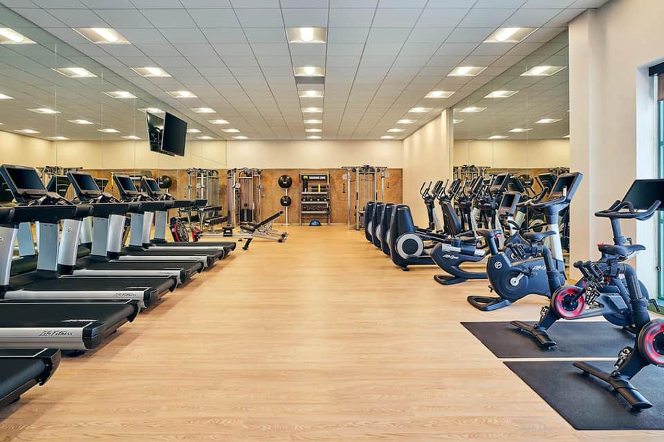 Modern fitness center with treadmills on left, stationary bikes on right, and weight equipment in center