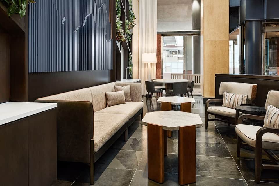 Modern hotel lobby with beige sectional sofa, wooden side tables, and contemporary black and tan decor