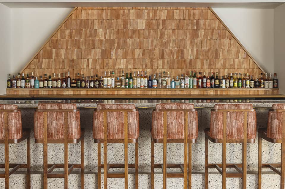 Bar counter with extensive liquor selection and wooden barstool seating with coral upholstery