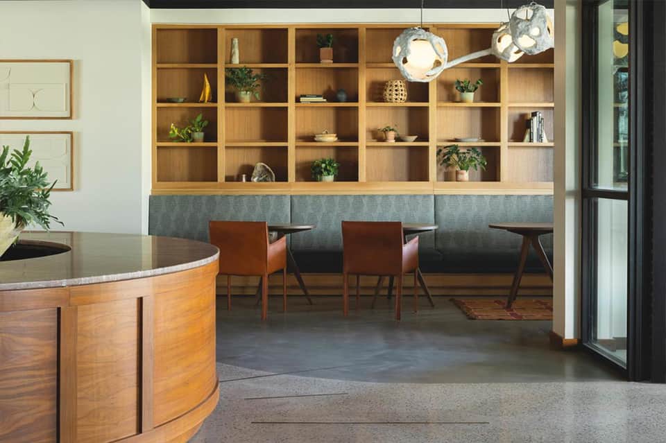 Modern hotel lobby with curved wooden reception desk, floor-to-ceiling shelving, and lounge seating