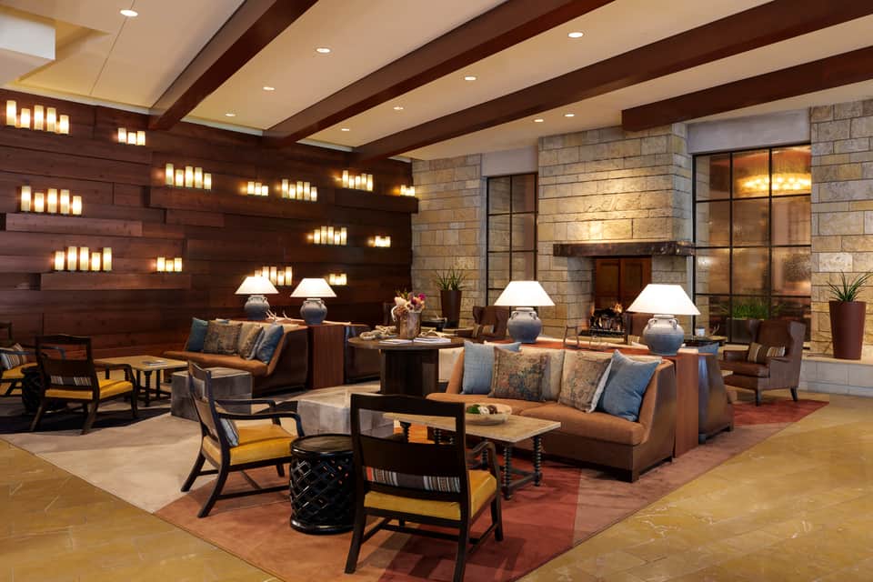 Elegant hotel lobby with dark wood accents, fireplace, brown leather seating, and decorative candle wall lighting