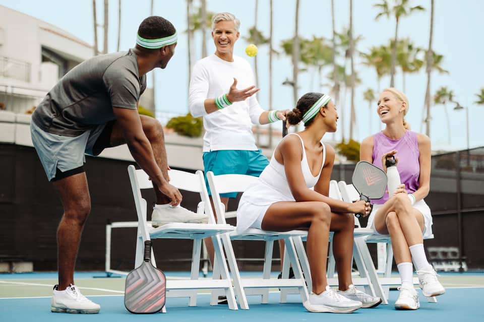Group of tennis players socializing on a sunny outdoor court with palm trees in background